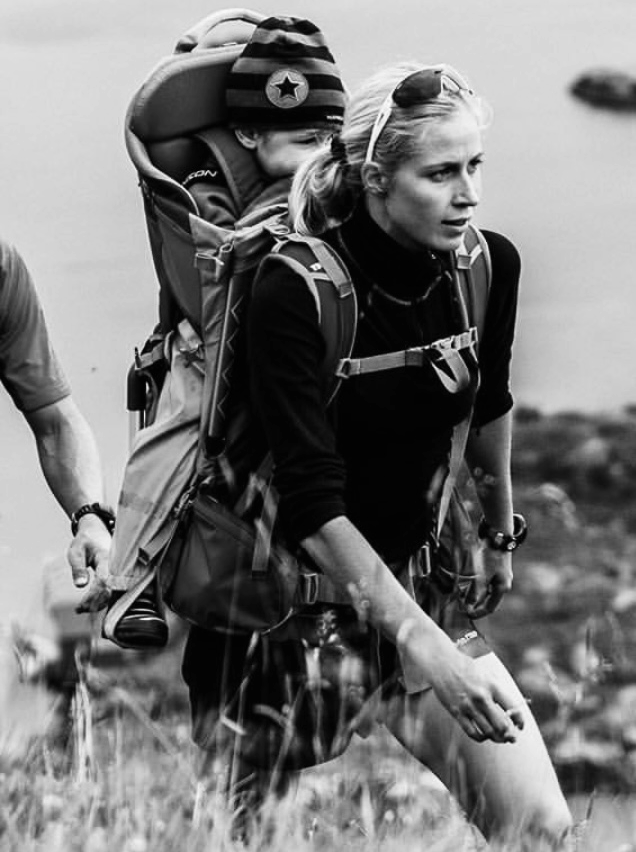KRISTIN LARsson hiking a coastal hillside carrying a child in a backpack carrier