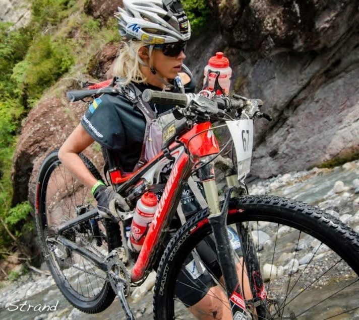 KRISTIN LARsson carrying her mountain bike across a rocky riverbed during a race
