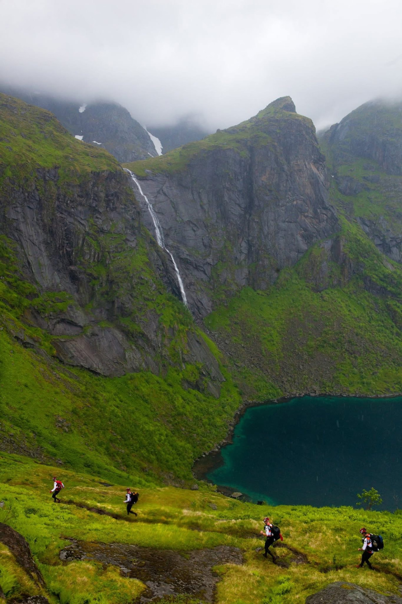 Adventure racers trekking across a green mountainside above a fjord